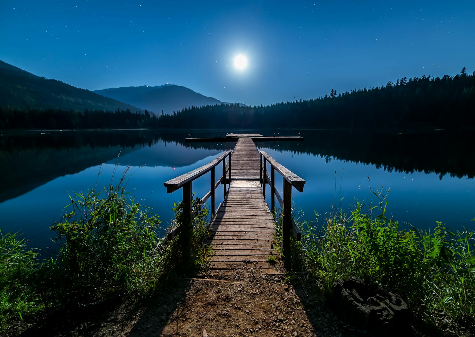 wooden dock over body of water, surrounded by mountains and fields